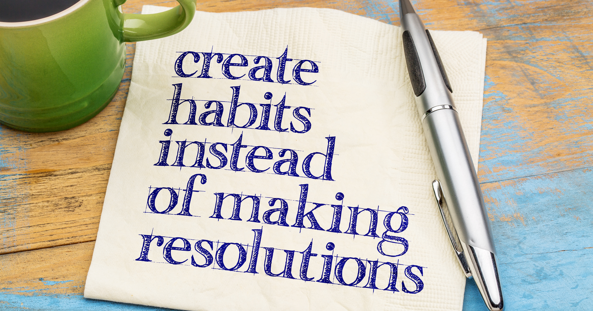 Don't make resolutions, create habits motivational reminder written on a napkin with a cup of coffee and a pen on the side.
